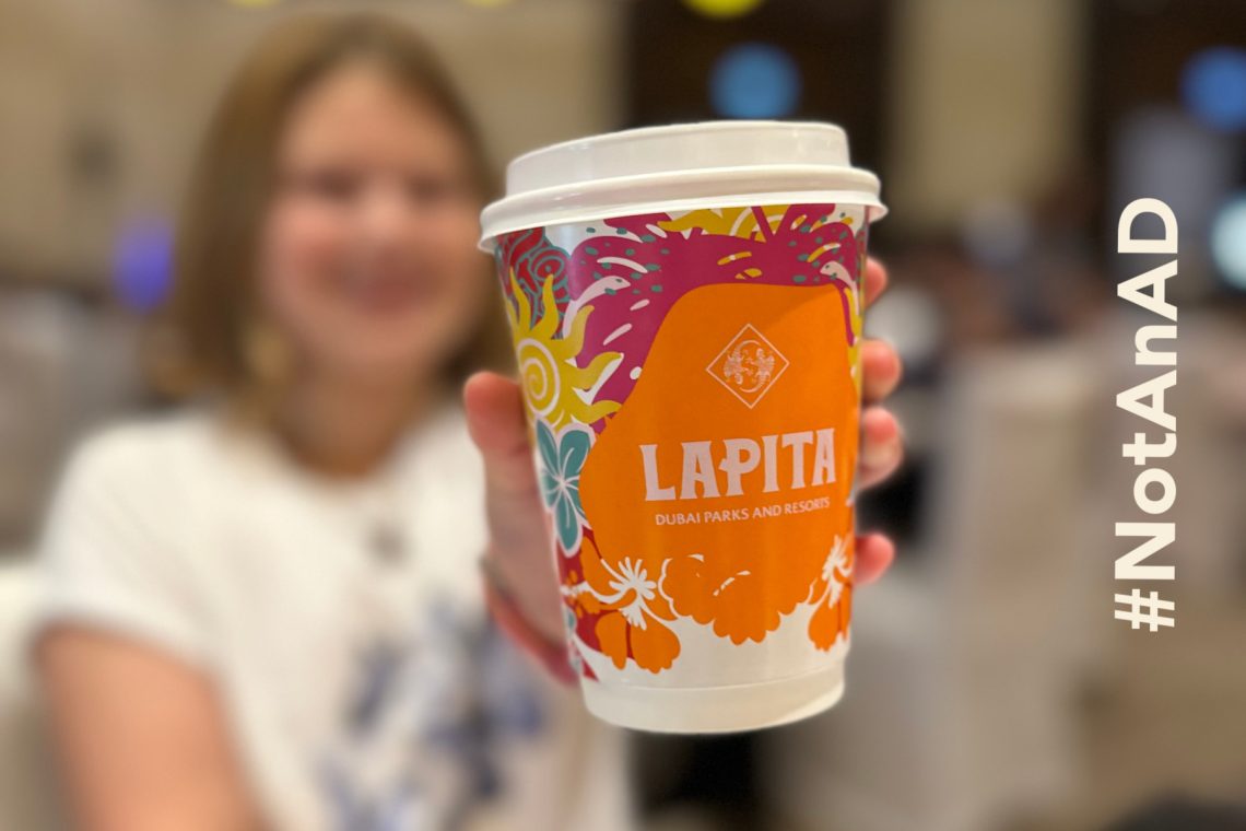 My daughter blurred in the background, She is holding a branded takeaway coffee cup which is in focus. On the right side there is overlayed text saying # Not an AD