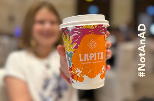 My daughter blurred in the background, She is holding a branded takeaway coffee cup which is in focus. On the right side there is overlayed text saying # Not an AD