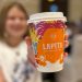 My daughter blurred in the background, She is holding a branded takeaway coffee cup which is in focus. On the right side there is overlayed text saying # Not an AD