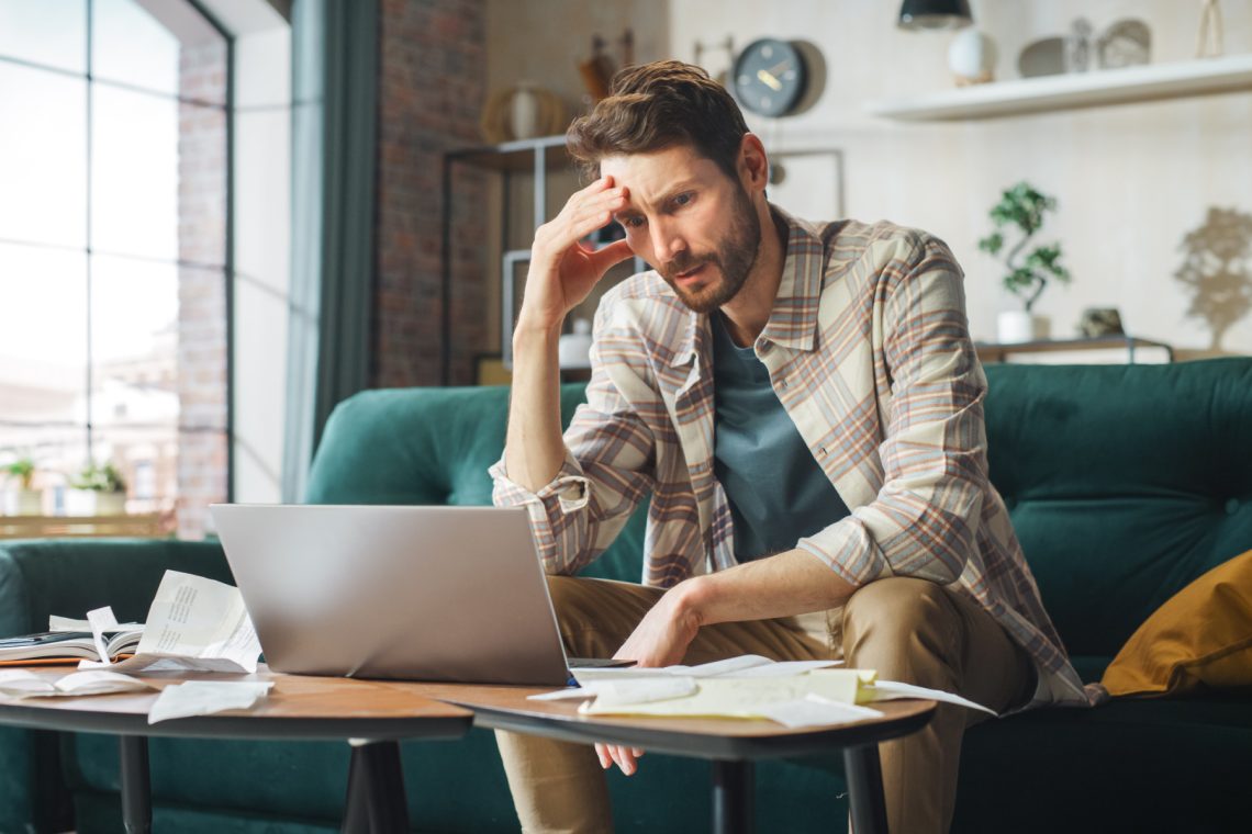 Stressful Accounting at Home: Man Using Laptop, Filling Tax Forms. Worried Male Has Paperwork Problems with Bills and Invoices. Budget Deficit, High Inflation, Financial Difficulty, Debt, Bankruptcy