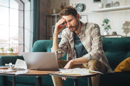 Stressful Accounting at Home: Man Using Laptop, Filling Tax Forms. Worried Male Has Paperwork Problems with Bills and Invoices. Budget Deficit, High Inflation, Financial Difficulty, Debt, Bankruptcy