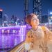 Happy woman blogger takes a beautiful selfie photo against the background of an artificial waterfall illuminated in neon light from a bridge in downtown Dubai. Social networks and travel in the UAE
