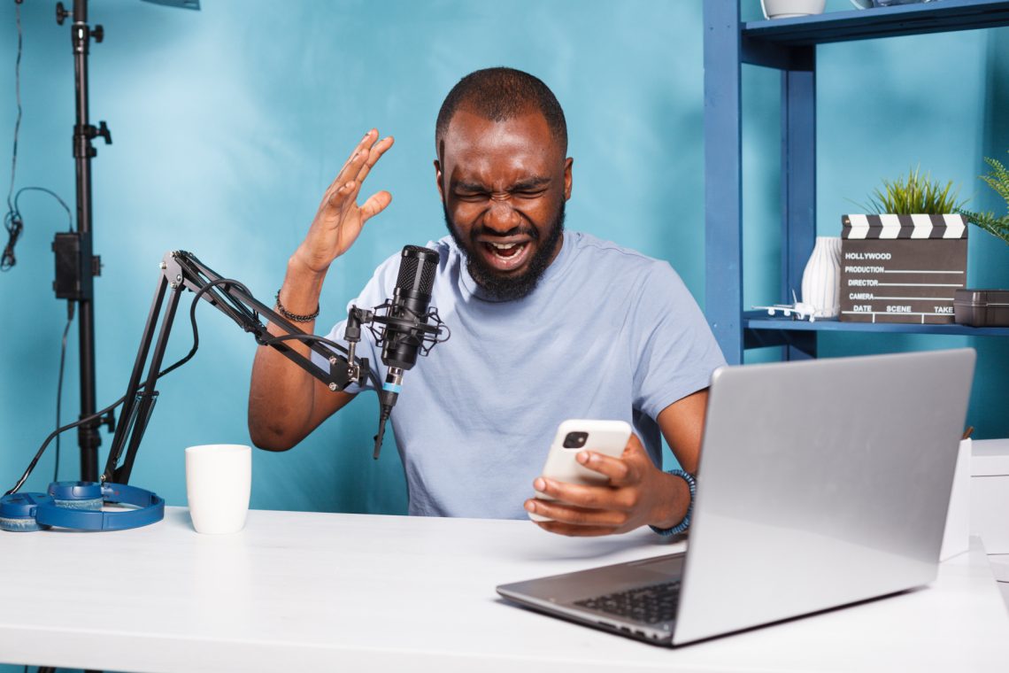 Furious african american blogger reading negative feedback on smartphone while recording video. Angry upset vlogger holding mobile phone and sharing bad news while streaming live